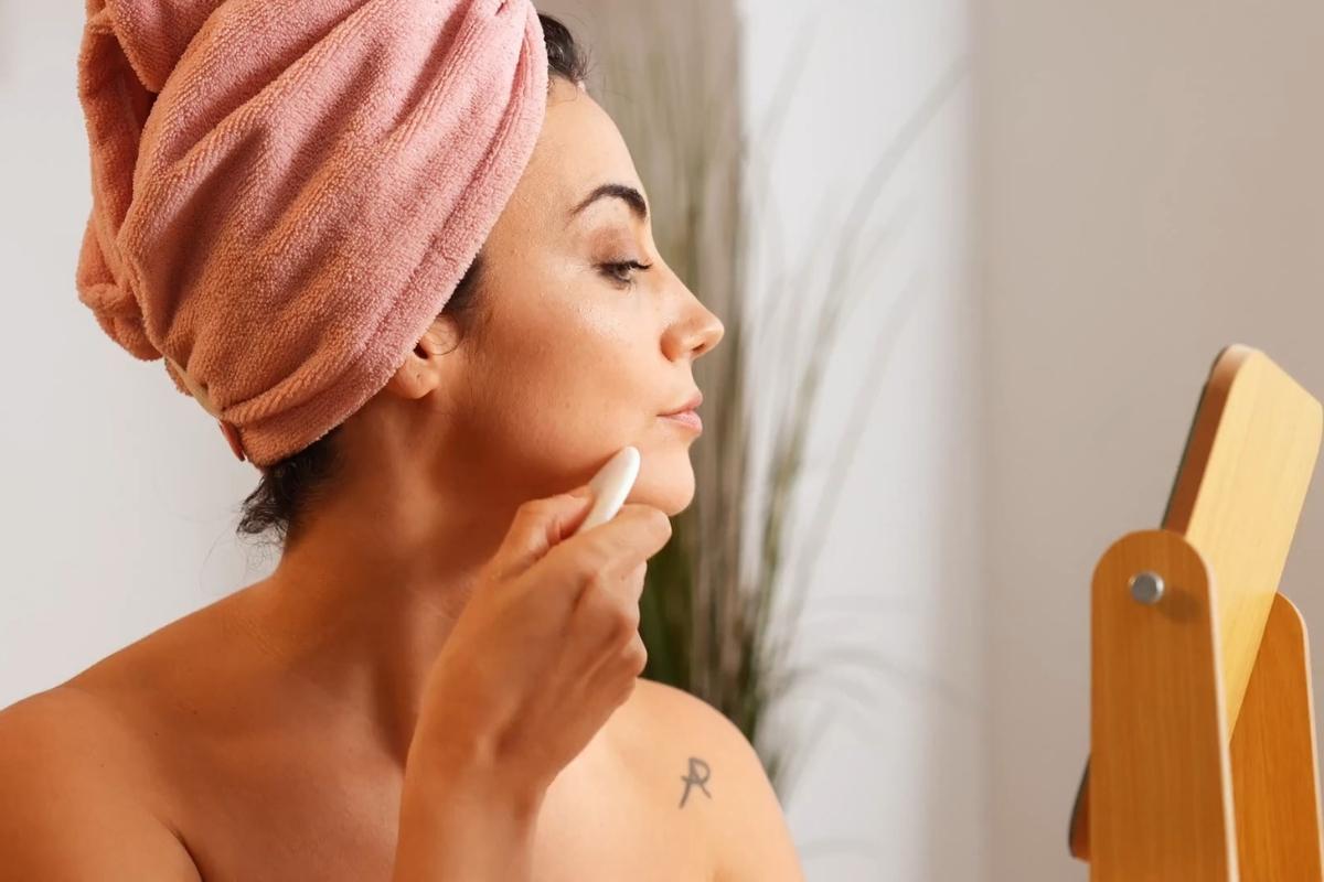 devojka sa peškirom na glavi radi Gua-sha masažu lica